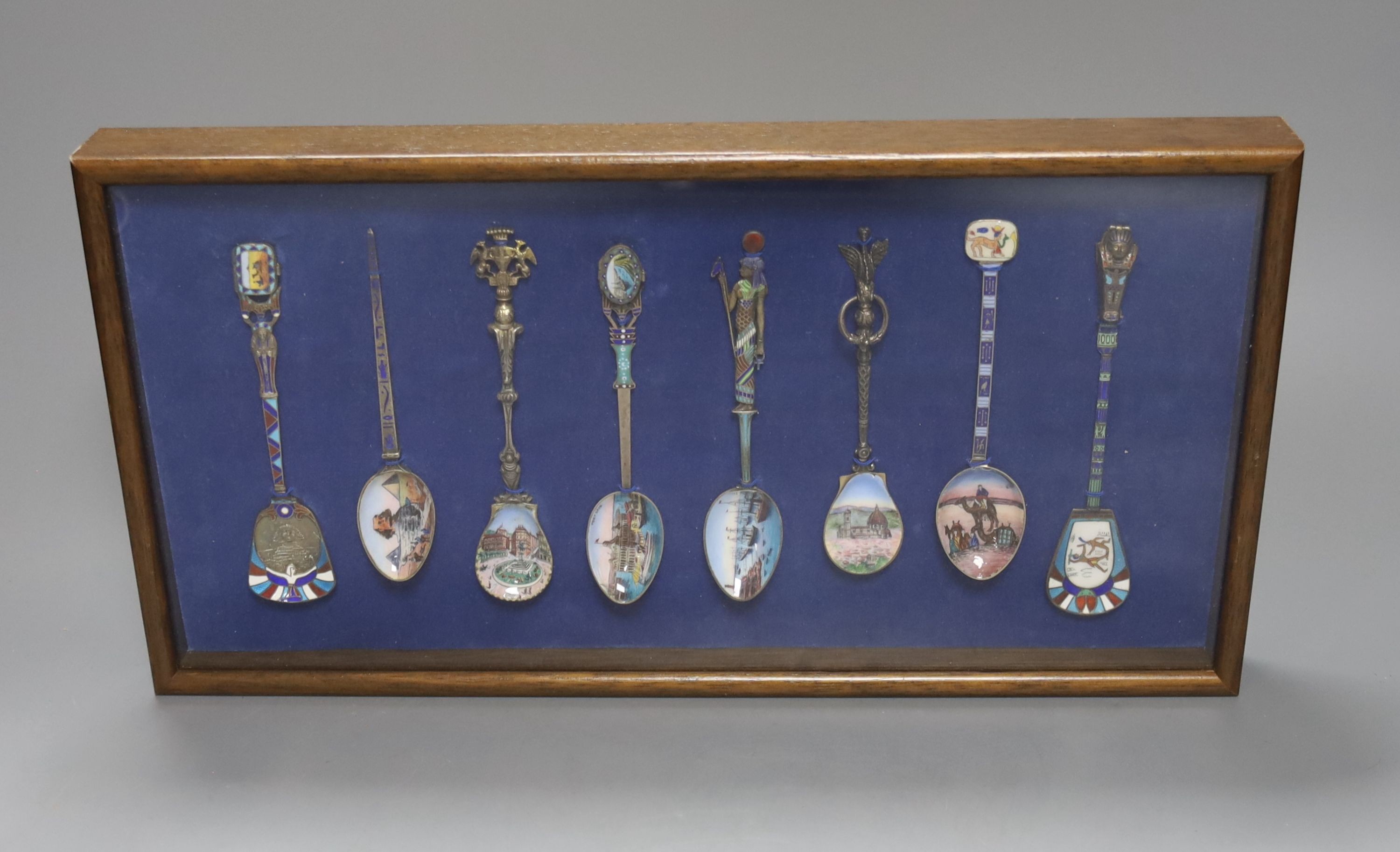 Eight Continental 800 standard silver and enamel ‘Egypt’ souvenir spoons, early 20th century, one with hinged sarcophagus terminal opening to reveal a small figure of a mummy, in a display case